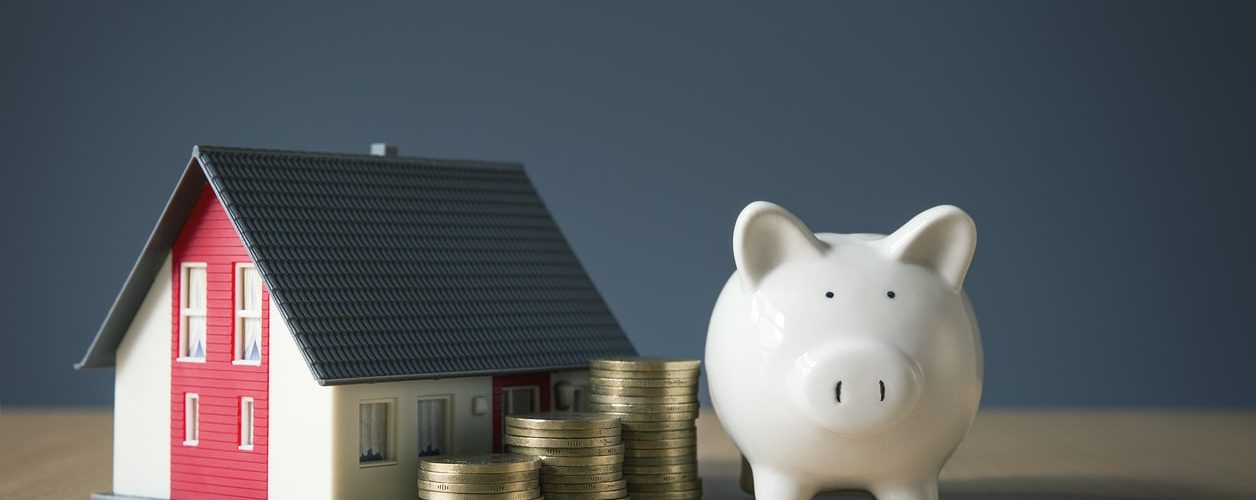 Piggybank resting beside a house as a visual representation of best financing options for roof replacement.