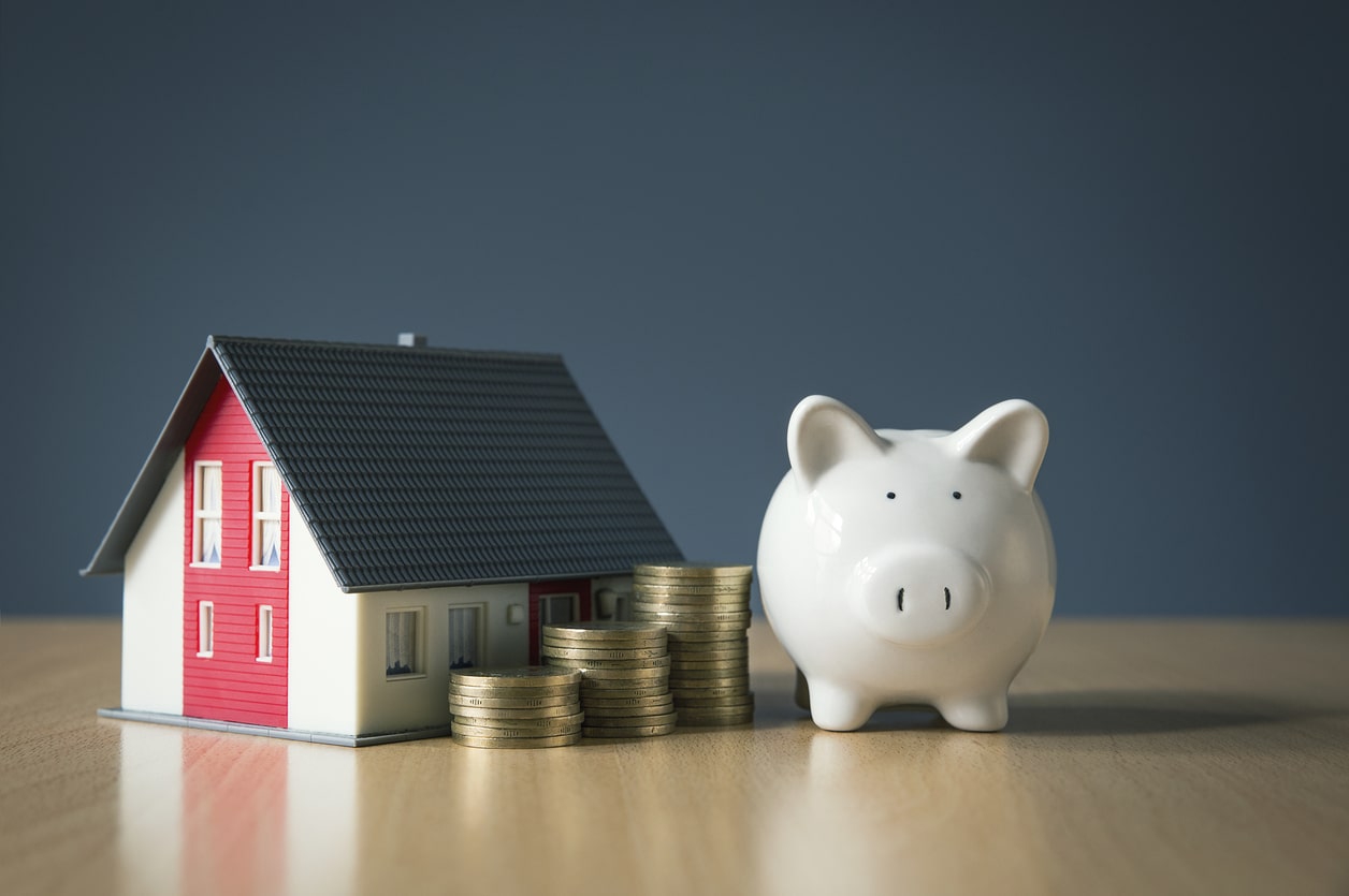 Piggybank resting beside a house as a visual representation of best financing options for roof replacement.